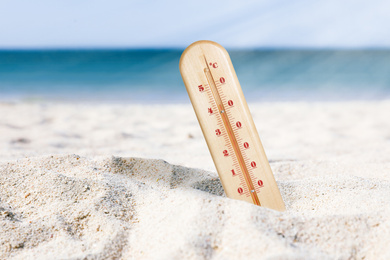 Weather thermometer with high temperature on sandy beach near sea