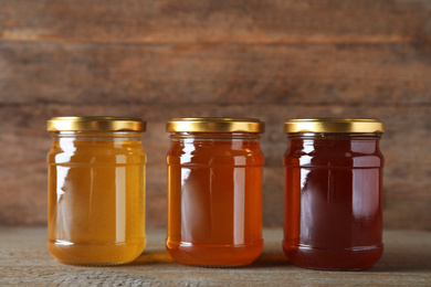 Jars with different types of organic honey on wooden table