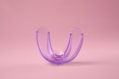 Photo of Transparent dental mouth guard on light pink background. Bite correction