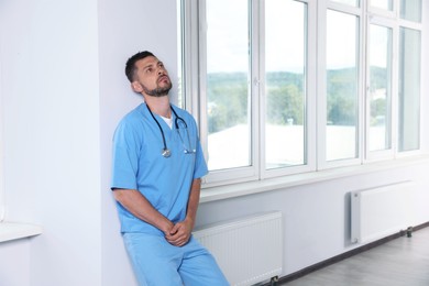 Exhausted doctor near white wall in hospital hallway