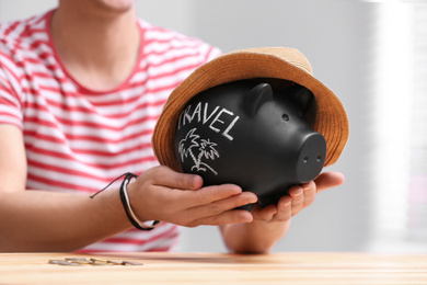 Man holding piggy bank with word TRAVEL and hat at table, closeup