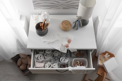 Modern open chest of drawers with baby clothes and accessories in room, above view