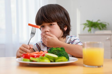 Cute little boy covering mouth and refusing to eat vegetables at home
