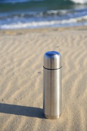 Photo of Metallic thermos with hot drink on sand near sea