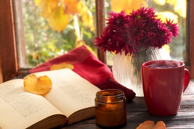 Photo of Beautiful chrysanthemum flowers, cup of hot drink and book on wooden table indoors. Autumn still life