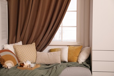 Comfortable lounge area with knitted blanket and soft pillows near window in room