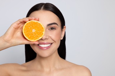 Photo of Woman holding half of orange on light grey background, space for text. Spa treatment