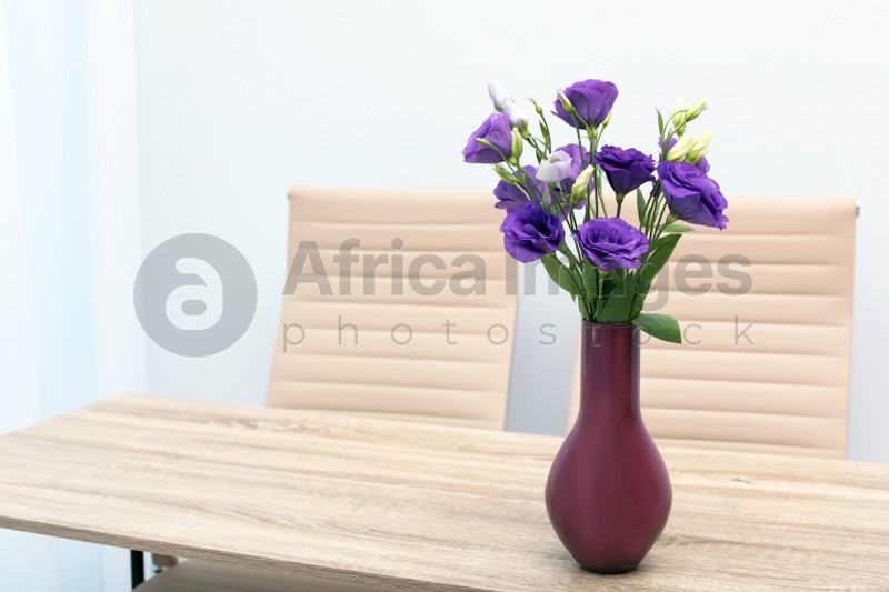 Beautiful bouquet in vase on wooden table against color background. Stylish interior