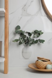 Silicone vase with eucalyptus branches on white marble wall over countertop in stylish bathroom