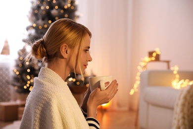 Young woman with cup of hot drink at home, space for text. Christmas celebration