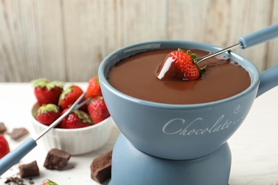 Dipping strawberry into fondue pot with chocolate, closeup