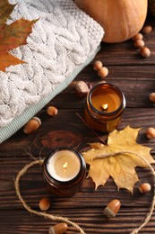 Burning scented candles, warm sweaters and acorns on wooden table. Autumn coziness