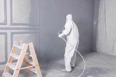 Photo of Decorator dyeing wall in grey color with spray paint indoors, back view