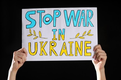 Photo of Teenage boy holding poster Stop War in Ukraine against black background, closeup
