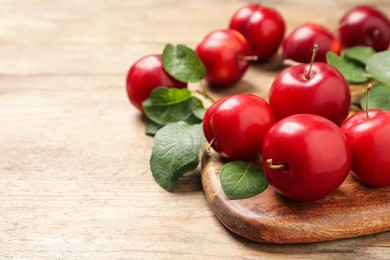 Delicious ripe cherry plums with leaves on wooden table, closeup. Space for text