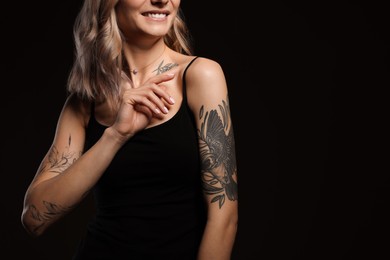 Beautiful woman with tattoos on body against black background, closeup. Space for text