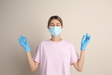 Woman in protective mask meditating on beige background. Dealing with stress caused by COVID‑19 pandemic