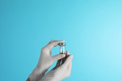Female doctor holding glass vial on color background, closeup view with space for text. Medical object