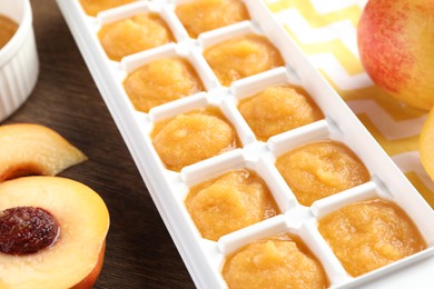 Photo of Nectarine puree in ice cube tray and fresh nectarine fruits on wooden table, closeup