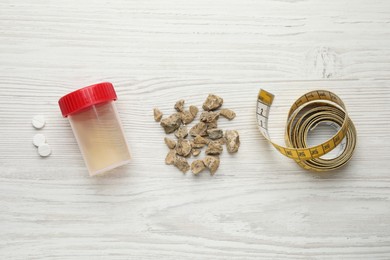 Kidney stones, jar of urine and measuring tape on white wooden table, flat lay
