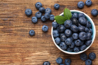 Tasty fresh blueberries and green leaves on wooden table, flat lay. Space for text