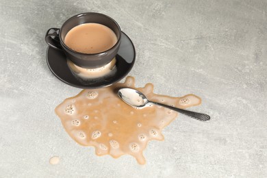 Cup, saucer and spoon near spilled coffee on grey table