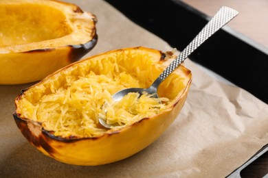 Halves of cooked spaghetti squash and spoon on baking sheet, closeup