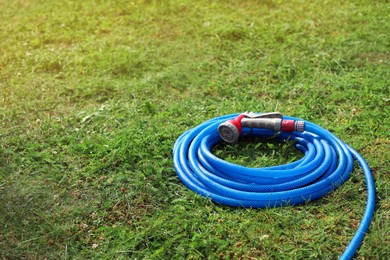 Photo of Watering hose with sprinkler on green grass outdoors, space for text