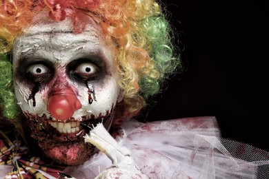 Photo of Portrait of terrifying clown on black background, closeup. Halloween party costume