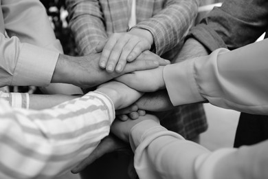 People holding hands together in office, closeup. Black and white effect