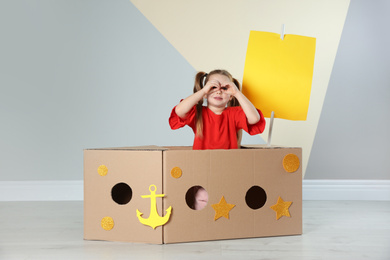 Cute little child playing with cardboard ship near color wall