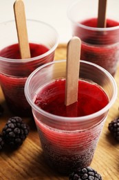 Tasty blackberry ice pops in plastic cups on table, closeup. Fruit popsicle