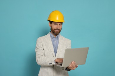 Professional engineer in hard hat with laptop on light blue background