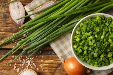 Chopped green onion in bowl on wooden table, flat lay