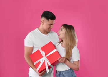 Man surprising his girlfriend with gift on pink background. Valentine's day celebration