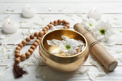 Golden singing bowl with flower, mallet and beads on white wooden table. Sound healing