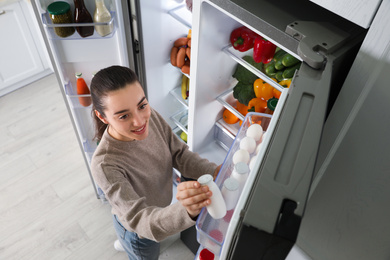 Young woman taking yoghurt out of refrigerator indoors, above view