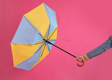 Man with umbrella caught in gust of wind on pink background, closeup