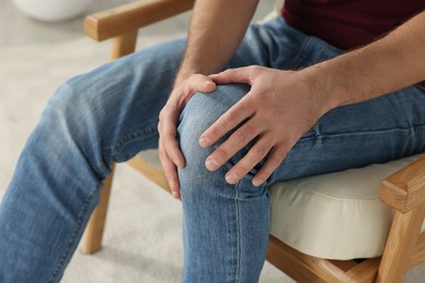 Photo of Man touching knee on soft armchair, closeup