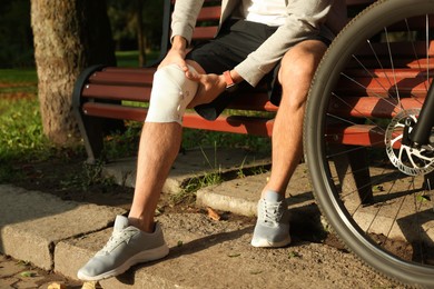 Man with injured knee on bench near bicycle outdoors, closeup