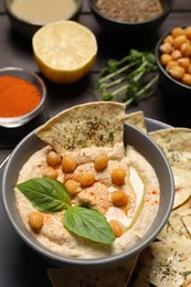 Photo of Delicious creamy hummus with chips and different ingredients on table, closeup