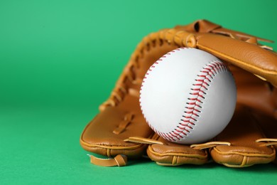 Photo of Catcher's mitt and baseball ball on green background, closeup with space for text. Sports game