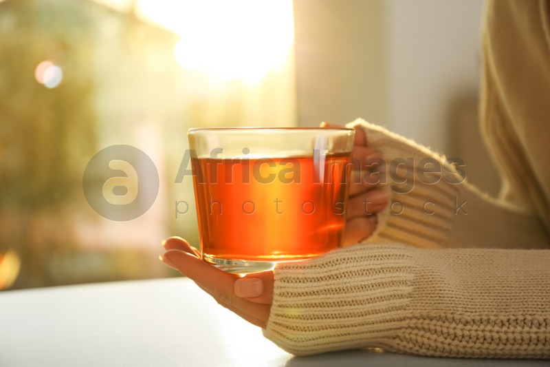 Woman holding glass cup of tea at table at home, closeup