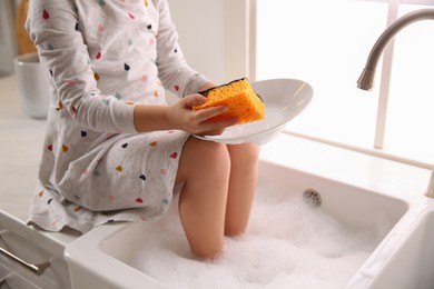 Naughty girl put her legs into sink while washing dishes in kitchen at home, closeup