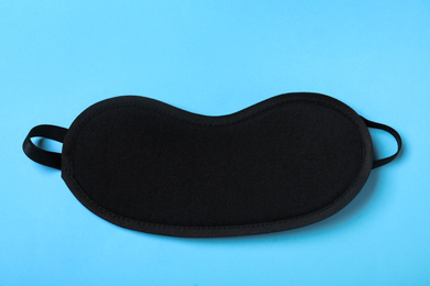 Black sleeping mask on light blue background, top view. Bedtime accessory