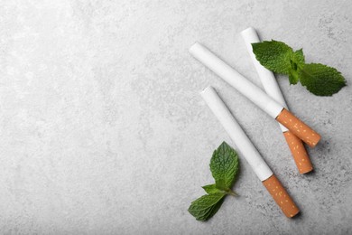 Menthol cigarettes and mint leaves on grey table, flat lay. Space for text