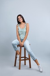 Beautiful young woman sitting on stool against light grey background