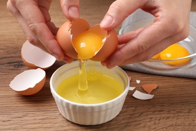 Photo of Woman separating egg yolk from white over bowl at wooden table, closeup