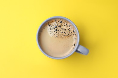 Grey mug of freshly brewed hot coffee on yellow background, top view