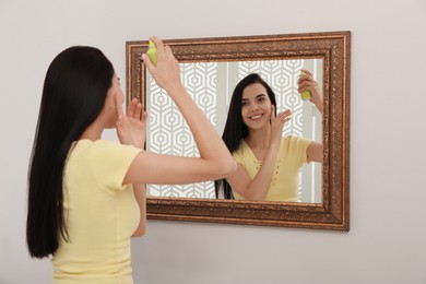 Woman applying dry shampoo onto her hair near mirror
